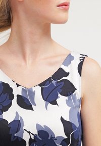 Vestido de estampado floral con cuello en V, con un fondo crema y flores azul oscuro. Confeccionado en un tejido suave y de diseño sin mangas.