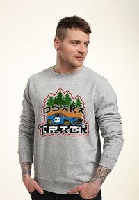 Grauer Sweatshirt mit einem grafischen Design eines blauen Autos und grünen Bäumen. Gerippte Bündchen und Saum. Siebdruckakzente in mehreren Farben.