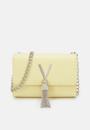 Petite pochette en cuir pastel jaune avec une bandoulière en chaîne argentée, fermoir en forme de V en argent et un détail de pompon argenté suspendu à l'avant.