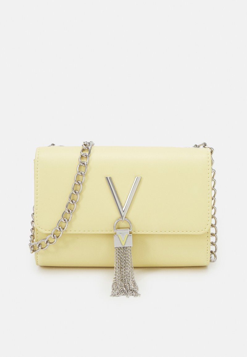 Liten pastellgul läderclutch med silverfärgad kedjeremm, V-formad silverfärgad lås och silverfärgad kvastdetalj hängande fram.