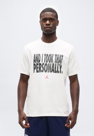 Jeune homme noir portant un T-shirt blanc avec le texte « AND I TOOK THAT PERSONALLY. » et un petit logo rouge Jordan, debout devant un fond clair uni.