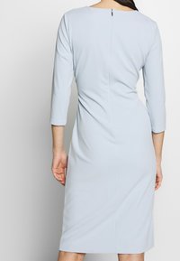 Ljusblå, figurnära klänning med trekvartslånga ärmar, rund halsringning och blixtlås i ryggen. Slät textur med diskret sidofålldesign.