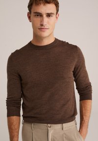 Pulover din tricot maro cu guler rotund, mâneci lungi și manșete dantelate, asortat cu pantaloni de culoare deschisă. Textură moale, design casual.