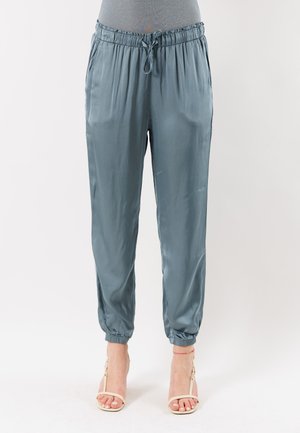 Pantaloni da jogging in seta blu con vita e polsini elastici, indossati con sandali beige con cinturini e tacco alto.