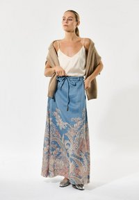 Maxi rok in lichtblauw met bloem- en paisleypatronen in roze en goud. Gecombineerd met een crème tanktop en een beige cardigan, zilveren slippers.