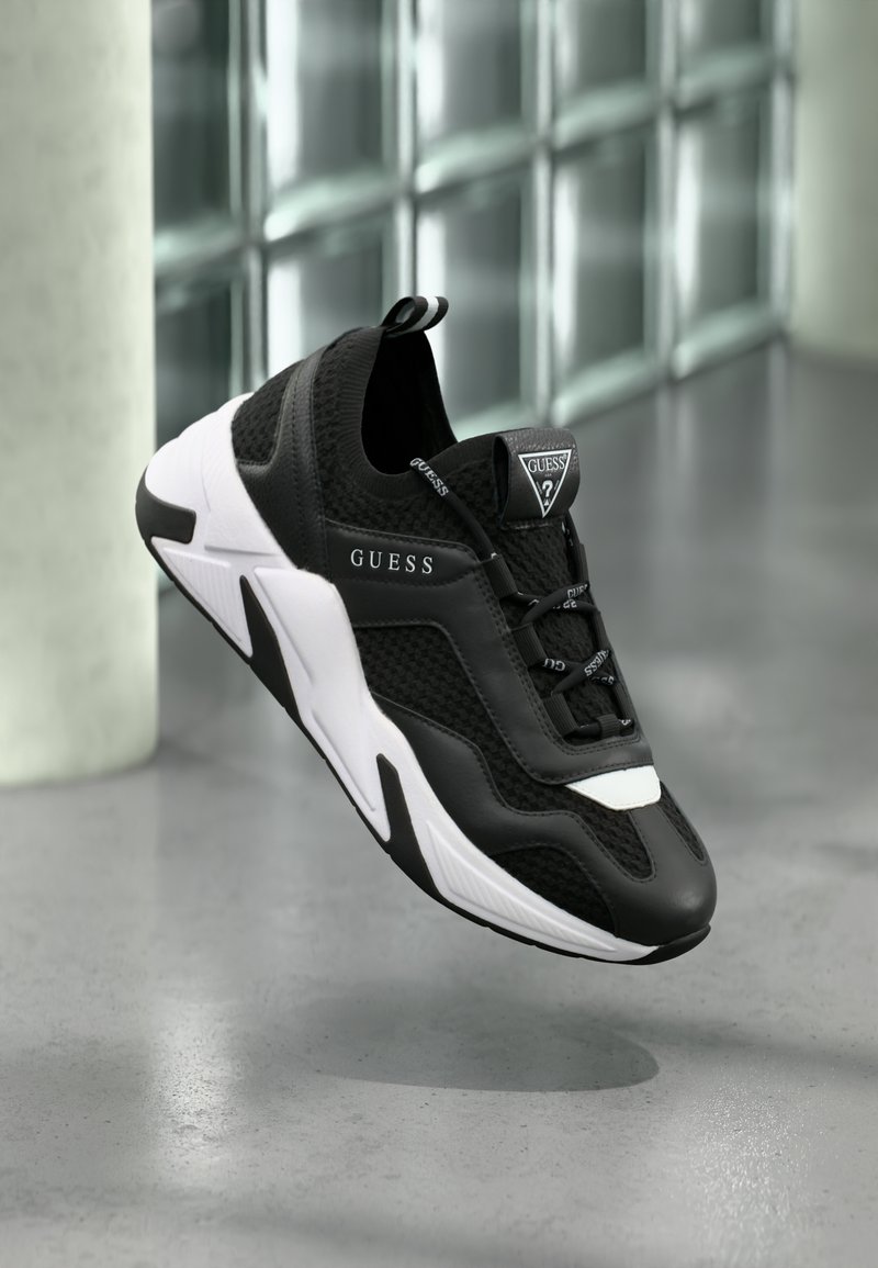 Black and white sneaker with mesh and synthetic materials, featuring a rounded toe, textured surface, and prominent logo accents.