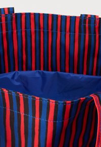 Εσωτερικό τσάντας με κάθετες ρίγες σε κόκκινο, μπλε και μαύρο και εσωτερική επένδυση σε σταθερό μπλε χρώμα που δείχνει ραφές και διπλωμένο ύφασμα.