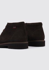 Botas de tobillo de ante marrón con un acabado texturizado, con puntera redonda, detalles de costura y suelas de goma. Etiqueta de logo pequeña en el lateral.