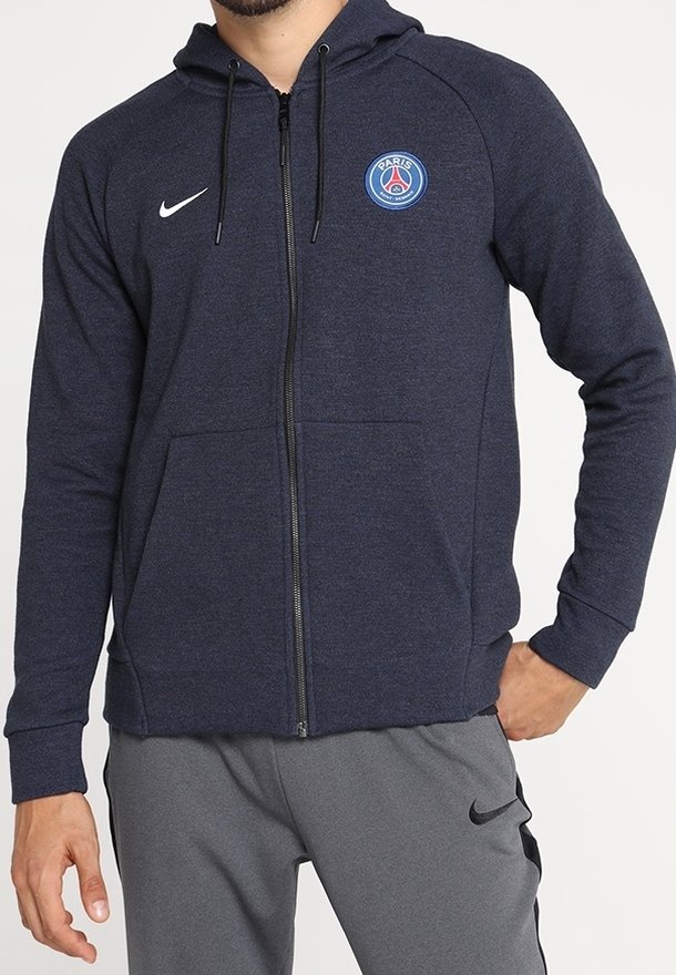 Sudadera con cremallera en azul marino, fabricada con un tejido suave, que presenta un logo del Paris Saint-Germain en el pecho y un swoosh de Nike en el lado izquierdo.