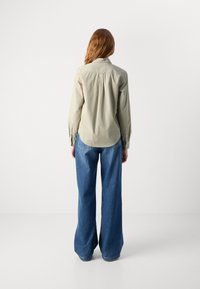 Light olive green button-up shirt with a rounded hem, paired with wide-leg blue denim jeans. The fabric appears smooth with subtle stitching details.