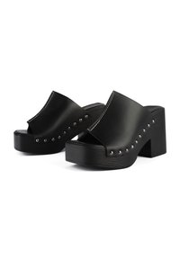 Black platform mules featuring wide straps, silver studs along the sides, and a textured block heel for added height and stability.