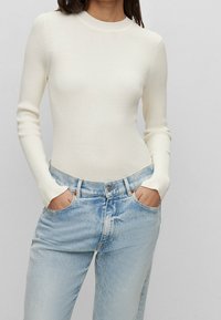 Vit ribbad långärmad topp kombinerad med ljusblå, blekta jeans. Toppen har hög krage och en figurnära silhuett.