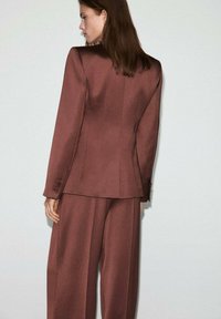 Hnedý prispôsobený blejzer so štruktúrovanými ramennými partami a zapínaním na jeden gombík, skombinovaný s voľnými nohavicami z rovnakého materiálu; textúrovaná tkanina.