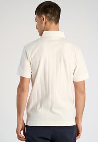 Biała koszulka polo z krótkim rękawem, charakteryzująca się pionowo prążkowaną teksturą, klasycznym kolorem i prostym wzornictwem.