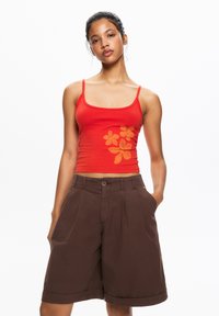 Red tank top with orange floral print; paired with brown, knee-length shorts featuring pockets and a button closure.