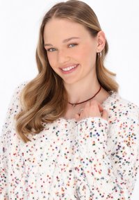 Witte, fuzzy trui met multicolore spikkels, voorzien van een brede halslijn en een losse pasvorm. Accessoires zijn een rode kralenketting.