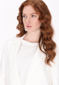 Sacou alb cu o croială lejeră, cu rever clasice și detalii minime, purtat peste o cămașă albă simplă. Textură moale și fluidă.