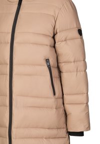 Beige gepolsterte Jacke mit einer strukturierten Oberfläche, ausgestattet mit einem schwarzen Reißverschluss, Seitentaschen und einem schwarzen Emblem am Ärmel. Das Design ist schlank.