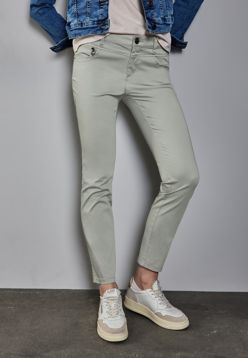 Lichtgrijze chinos met een slim fit, voorzien van voorzakken en een nauwsluitend ontwerp, gecombineerd met witte en beige sneakers.