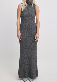 Abito lungo senza maniche grigio a maglia con collo alto, caratterizzato da una silhouette aderente e una texture a coste, abbinato a tacchi blu.