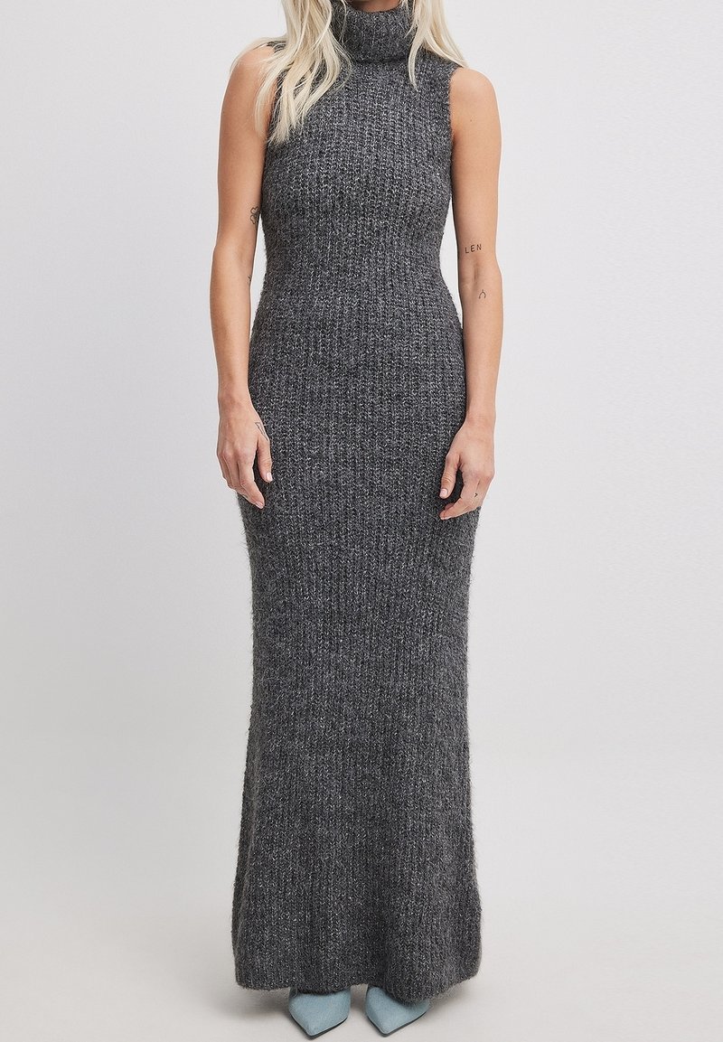 Abito lungo senza maniche grigio a maglia con collo alto, caratterizzato da una silhouette aderente e una texture a coste, abbinato a tacchi blu.