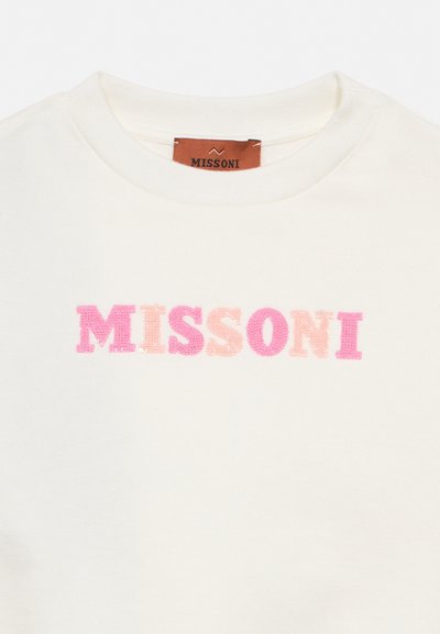 Λευκό ένδυμα με στρογγυλή λαιμόκοψη και ροζ και ροδακινί παγιέτες που σχηματίζουν τα γράμματα «MISSONI» και καφέ ετικέτα ραμμένη στο εσωτερικό του γιακά.