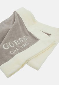 Grå og creme vendbar tæppe med blød tekstur. Har broderet "GUESS" og "CAL. 1981" på den grå side.