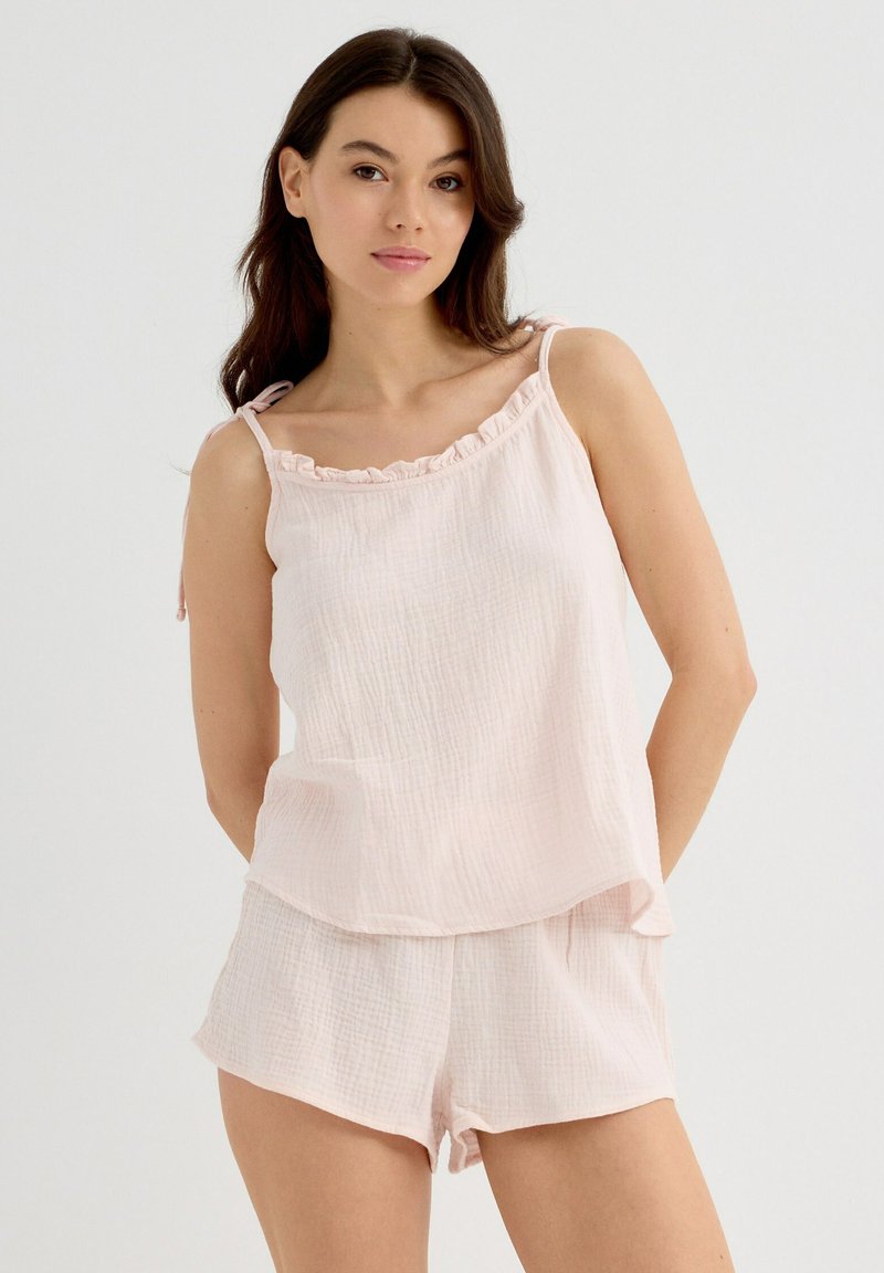 Conjunto de pijama rosa claro que incluye una parte superior sin mangas con cuello rizado y pantalones cortos de corte holgado, fabricado con un material texturizado y suave.