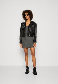Chaqueta de motociclista de cuero negro corta sobre un vestido de punto gris. El atuendo se complementa con zapatos gruesos negros y gafas de sol negras.