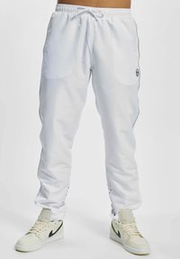 Weiße Sporthosen mit elastischem Bund, versehen mit schwarzen Akzentlinien und Seitentaschen. Kombiniert mit hellen Sneakers.