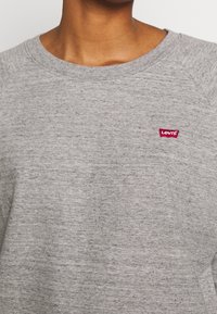 Sudadera gris hecha de un tejido texturizado. Presenta un escote redondo y un pequeño logo rojo de Levi's en el pecho.