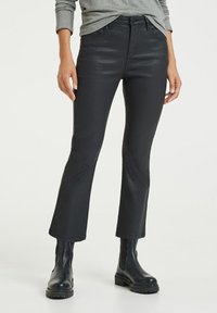 Svarta utsvängda jeans gjorda av ett stretchigt, glänsande material, med klassisk femfickdesign och bältesöglor, kombinerade med svarta ankelskor.