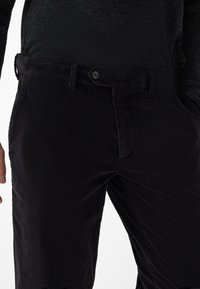 Zwarte corduroybroeken met een gestructureerd oppervlak, voorzien van een knoopsluiting en riemlussen, weergegeven in een middelhoge taille.