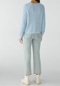 Vaaleansininen neulepaita, jossa on resorikuvio, yhdistetty vaaleisiin farkkuihin. Asu viimeistellään massiivisilla valkoisilla nilkkureilla.