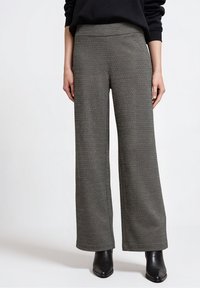 Pantalones de pierna ancha en una tela texturizada de color gris oscuro. Cuenta con una cintura lisa y detalles de costura mínimos, combinados con botines negros hasta el tobillo.