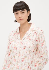 Camisa de pijama com padrão floral em tecido leve, apresentando uma base branca com flores rosa e verdes, gola e detalhe de bolso frontal.