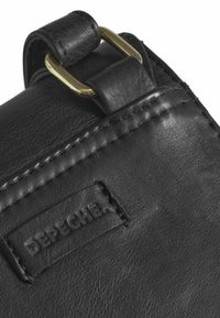 Bolso de cuero negro con una superficie texturizada, presenta una hebilla en tono dorado y una etiqueta DEPECHE cosida. Diseño compacto y herrajes funcionales.