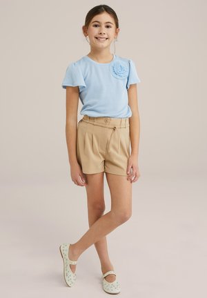 Camisa de manga corta de rayas azul claro con detalle de flor, combinada con pantalones cortos plisados de talle alto en beige y zapatos verde claro con acentos.