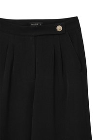Pantaloni neri su misura con pieghe frontali, tasche laterali e un bottone metallico decorativo in vita. Etichetta del marchio visibile all'interno.