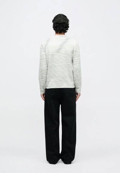 Gaiši pelēks teksturēts džemperis ar garām piedurknēm, kopā ar vaļīgām melnām biksēm. Džemperim ir horizontālas svītras un apaļa izgriezuma kakls.