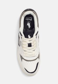 Zapatilla blanca y gris con un upper de cuero, acentos en negro y cordones claros. Presenta un logo en la lengüeta y una plantilla texturizada.