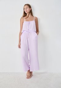 Lavendel tweedelig outfit met een losvallende top met verstelbare bandjes en een drawstring taille, gecombineerd met wijde broekspijpen.