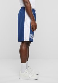 Blå træningsshorts med hvide sidepaneler, prydet med et logo. Båret med hvide sneakers og ankelsokker. Glat stofstruktur.
