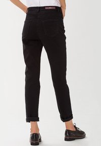 Jeans de mezclilla negra con perneras rectas, puños enrollados y dos bolsillos traseros, que cuentan con una cinturilla de marca y una tela texturizada.