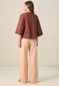 Brauner kurzer Oberteil mit goldener Muschelstickerei und weiten Ärmeln. Kombiniert mit hellrosa Schlaghosen, die über Taschen auf der Rückseite und einen sauberen Saum verfügen.