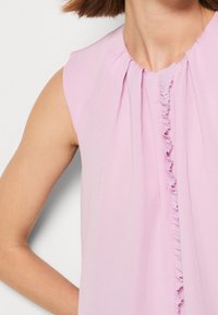 Vestido sin mangas rosa con detalle fruncido en la parte delantera, hecho de una tela ligera. El escote es redondo con suaves pliegues a lo largo de los hombros.
