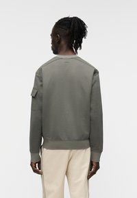  Φούτερ σε ελιά πράσινο χρώμα με στρογγυλή λαιμόκοψη, ριμπ μανσέτες και τελείωμα, που διαθέτει τσέπη στον ώμο και διακριτικό λογότυπο "BOSS" στο πίσω μέρος.