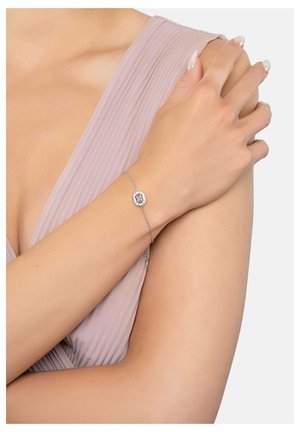 Delicate silver chain bracelet featuring a central pink gemstone surrounded by small clear stones worn on a wrist with a mauve pleated sleeveless top.
