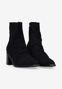 Botines de ante negro con un diseño holgado, puntera afilada y un tacón cuadrado medio. Cuenta con una cremallera lateral para facilitar el uso.