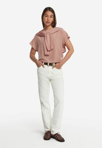 Ljusröd blus med knut vid halsen, kombinerad med vita raka jeans och bruna sandaler med remmar, samt ett brunt bälte.